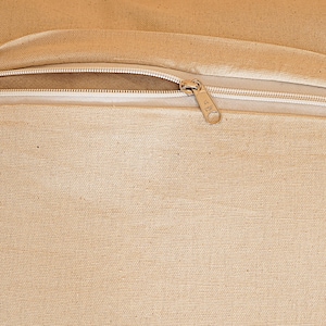 May include: Close-up of a beige canvas fabric with a white zipper. The zipper is open, revealing the interior of the fabric. The zipper pull is gold-colored.