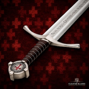 May include: A silver-toned metal sword featuring a dark brown leather-wrapped grip and a crossguard. The pommel displays a circular emblem with a red cross. The blade is engraved with the Latin text NON NOBIS DOMINE NON NOBIS SED.