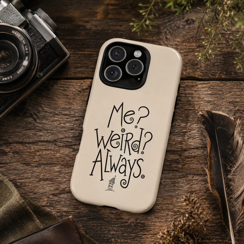 May include: A cream-coloured smartphone case featuring the black text "Me? Weird? Always." written in a stylised, swirling font. Below the text is a small, simple line drawing of a house. The case has a black camera cutout for three lenses.