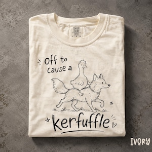 Könnte beinhalten: Ein elfenbeinfarbenes Kurzarm-T-Shirt mit einer schwarzen Strichzeichnung einer Ente, die auf dem Rücken eines Hundes reitet. Der Text lautet "Off to cause a kerfuffle" mit kleinen Stern- und Herzakzenten. Das Shirt hat einen Rundhalsausschnitt.