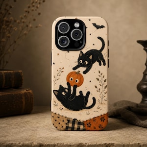 Könnte beinhalten: Eine cremefarbene Handyhülle mit einer gedruckten Illustration von zwei schwarzen Katzen, die mit einem orangefarbenen Kürbis spielen. Das Design enthält kleine Sterne, eine Fledermaus und botanische Elemente sowie eine Bordüre im Patchwork-Stil.