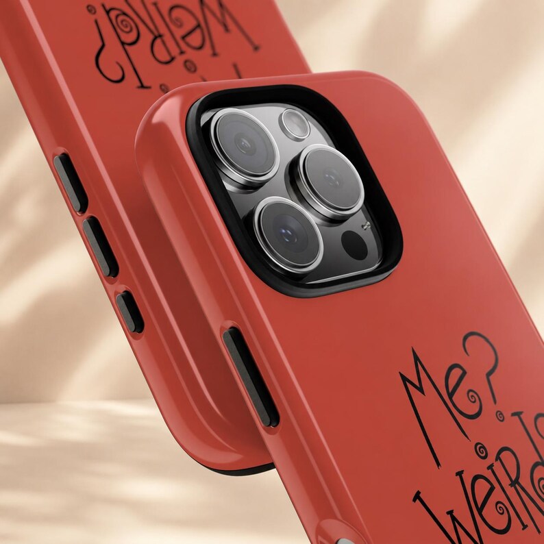 May include: A red smartphone case with a black camera module and black side buttons. The back of the case features the black text "Me? Weird?" written in a stylised, swirling font. The case has a smooth, matte finish and a protective raised edge.