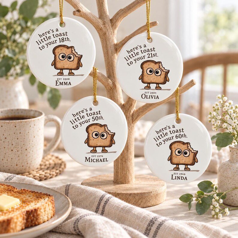 May include: Four round white ceramic ornaments hanging from a wooden stand. Each features a cartoon slice of toast with eyes and limbs, the text "here's a little toast to your [age]th.", a birth year, and a name: Emma, Olivia, Michael, or Linda.