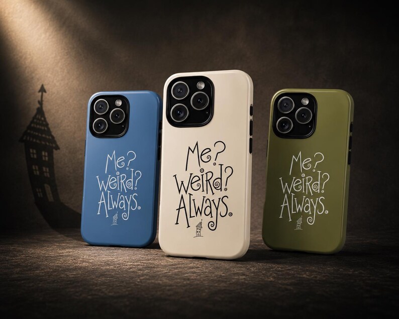 May include: Three smartphone cases in blue, cream, and olive green. Each case features a black camera module and the printed text "Me? weird? Always." in a stylised font, accompanied by a small illustration of a house at the bottom.