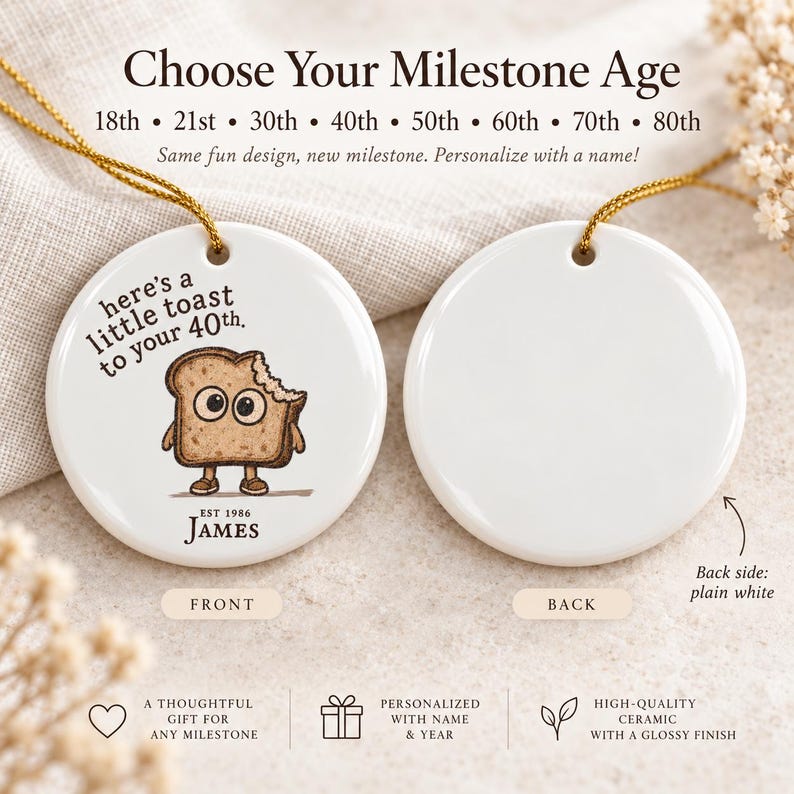 May include: Two round white ceramic ornaments with gold hanging strings. The left ornament features a cartoon toast character with the text 'here's a little toast to your 40th.' and 'EST 1986 JAMES'. The right ornament is plain white on both sides.