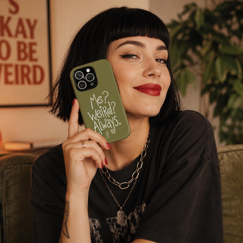 May include: An olive green smartphone case featuring a triple camera cutout and the white printed text "Me? WEIRD? Always." in a stylised, handwritten font. The case has a smooth matte finish and covers the back of the mobile device.
