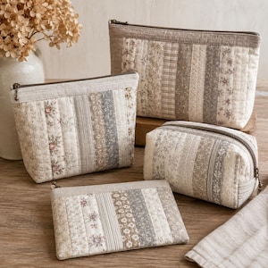 Puede incluir: Un conjunto de cuatro estuches acolchados de varios tama&ntilde;os, cada uno con un dise&ntilde;o de patchwork vertical de tiras de tela en beige, gris y blanco con patrones florales y de rayas. Cada estuche cuenta con una cremallera y un tirador met&aacute;lico.