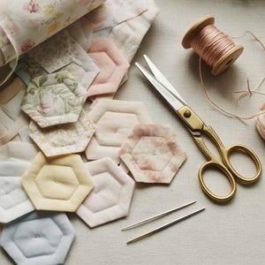 May include: A selection of quilting tools and materials. Hexagon-shaped fabric pieces in pastel shades, gold scissors, needles, and a spool of pink thread are arranged with floral fabric and a quilt.