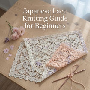 Op de afbeelding: Een houten tafel toont een Japanse kanten breigids voor beginners. Twee stukken delicate kant, één crème en de andere perzik, zijn opgevouwen. Breinaalden en bloemen zijn in de buurt gerangschikt. De tekst op de gids is zichtbaar.
