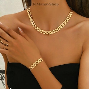 Puede incluir: Un conjunto de joyas de color dorado con un collar y una pulsera. El collar está alrededor del cuello y la pulsera en la muñeca. Las joyas tienen un diseño de eslabones rectangulares. El nombre de la tienda "EfeManavShop" está en la esquina superior izquierda.