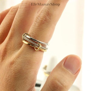 Pode incluir: Um anel multicolorido com detalhes em ouro, prata e diamantes. O anel apresenta um design único com faixas interligadas. O texto "EfeManavShop" é visível na parte superior da imagem.