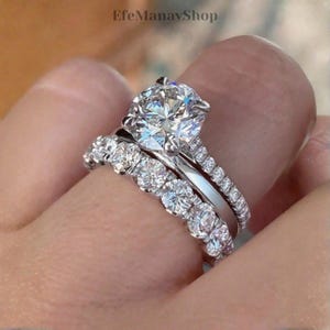 Puede incluir: Un juego de anillos de diamantes de tres piezas. El anillo de compromiso presenta un diamante grande de talla redonda. La alianza y el anillo adicional están adornados con diamantes más pequeños, engastados en una banda plateada.