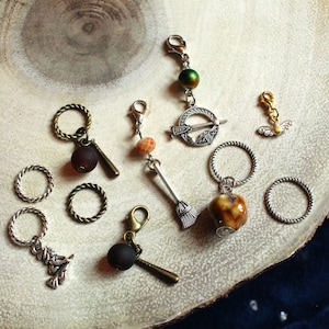 May include: A collection of 10 charm beads for jewelry making. The charms include a broom, a potion bottle, a tree, a bee, an arrow, and a few round beads. The charms are silver, gold, and brown in color.