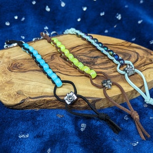 May include: Three beaded keychains with different colored beads and charms. The keychain on the left has light blue beads and a camera charm. The keychain in the middle has yellow beads and a flower charm. The keychain on the right has iridescent blue beads and a crown charm.