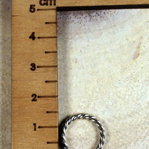 Może przedstawiać: Srebrny pierścionek z plecionym wzorem, zmierzony za pomocą linijki z oznaczeniami w calach i centymetrach. Linijka jest oznaczona jako "knitters".