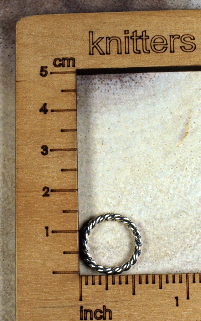 Może przedstawiać: Srebrny pierścionek z plecionym wzorem, zmierzony za pomocą linijki z oznaczeniami w calach i centymetrach. Linijka jest oznaczona jako "knitters".