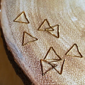 May include: A collection of small gold triangle-shaped metal hoops on a wooden surface.