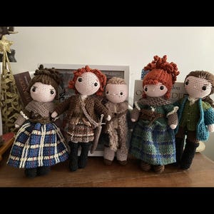 May include: Five handmade crochet dolls, each with unique outfits and hairstyles. The dolls have light skin and are dressed in various outfits, including plaid skirts, jackets, and shawls. The dolls have different hair colors, including brown and red.