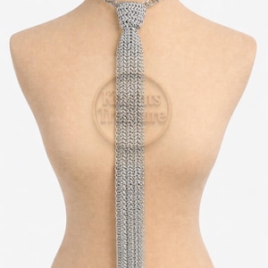 May include: A silver-colored chain tie displayed on a mannequin. The tie features a woven design for the knot and a long, fringed tail. The chain is connected to a necklace-style chain that goes around the neck. The tie is a unique accessory.