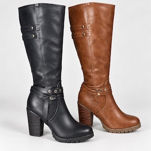 May include: A pair of knee-high boots, one black and one tan, featuring a stacked block heel, a lugged sole, and a decorative strap across the ankle with metallic studs. Each boot has a vertical strap detail near the top with two metallic rivets.