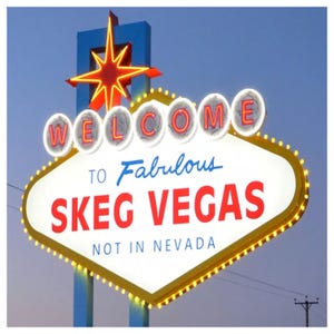 May include: A neon sign with the words "WELCOME TO Fabulous SKEG VEGAS NOT IN NEVADA". The sign is white with red lettering and a yellow border. A red starburst sits atop a blue structure.