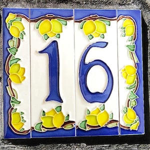 Puede incluir: Número dieciséis de casa de cerámica decorativa. El número está en una fuente azul negrita, sobre un fondo blanco. Las baldosas están enmarcadas con un borde azul y adornadas con limones amarillos y hojas verdes.
