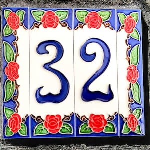 May include: Decorative ceramic house number tile featuring the number "32" in a bold, dark blue font. The tile is white with a blue border adorned with red roses and green leaves. A charming addition to any home.