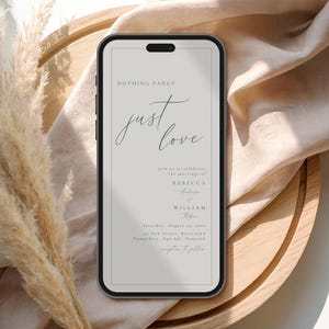 Op de afbeelding: Een smartphone toont een huwelijksuitnodiging met de tekst "NOTHING FANCY just love." De uitnodiging bevat de namen Rebecca Anderson en William Riber, de trouwdatum en -locatie. De telefoon ligt op een houten dienblad.
