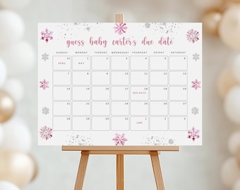 Op de afbeelding: Een witte kalenderbord op een houten ezel, met roze en zilveren sneeuwvlokontwerpen. De tekst luidt "guess baby carter's due date" met een kalenderraster voor april, mei en juni. De ezel is gemaakt van lichtbruin hout.