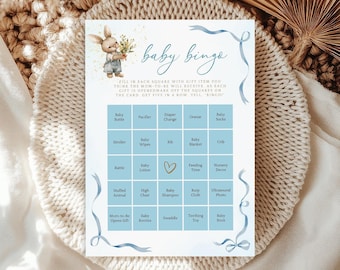 May include: A baby bingo game card with a watercolor illustration of a bunny holding flowers. The card has a blue ribbon design and includes squares with baby-related items like diapers, bottles, and toys. The text "baby bingo" is written in cursive.