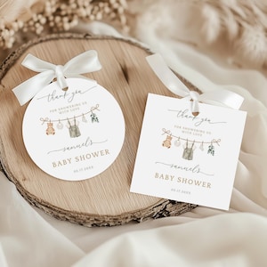 Puede incluir: Dos etiquetas de recuerdo de baby shower, una redonda y otra cuadrada, con cinta blanca. Las etiquetas presentan una ilustración de acuarela de ropa y juguetes de bebé colgados de un tendedero. El texto dice "gracias", "Baby Shower" y "Samuels".