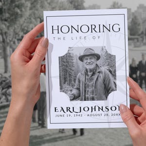 Könnte beinhalten: Eine schwarz-weiße Gedenkkarte, die von Händen gehalten wird. Die Karte trägt die Aufschrift "HONORING THE LIFE OF EARL JOHNSON" mit einem Foto eines lächelnden Mannes mit Hut. Die Daten "JUNE 19, 1942 - AUGUST 28, 20XX" sind darunter abgedruckt.