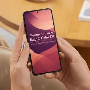 May include: A smartphone screen shows the text "Perimenopause Rage & Calm Kit" with a red and purple graphic. The phone is held in two hands. The background is blurred.
