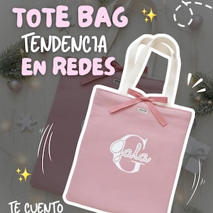 Puede incluir: Dos bolsas tote rosas con asas y lazos blancos. Una bolsa tiene el nombre "Gala" en escritura blanca. El texto de la imagen dice "Tote Bag Tendencia en Redes" y "Te cuento por qué". Las bolsas están sobre un fondo claro con elementos decorativos.