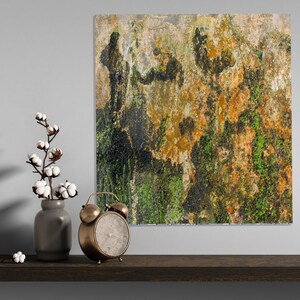May include: A square abstract art piece with a textured surface, featuring shades of orange, green, and brown. A vintage brass alarm clock and a gray vase with cotton stems are on a wooden shelf.