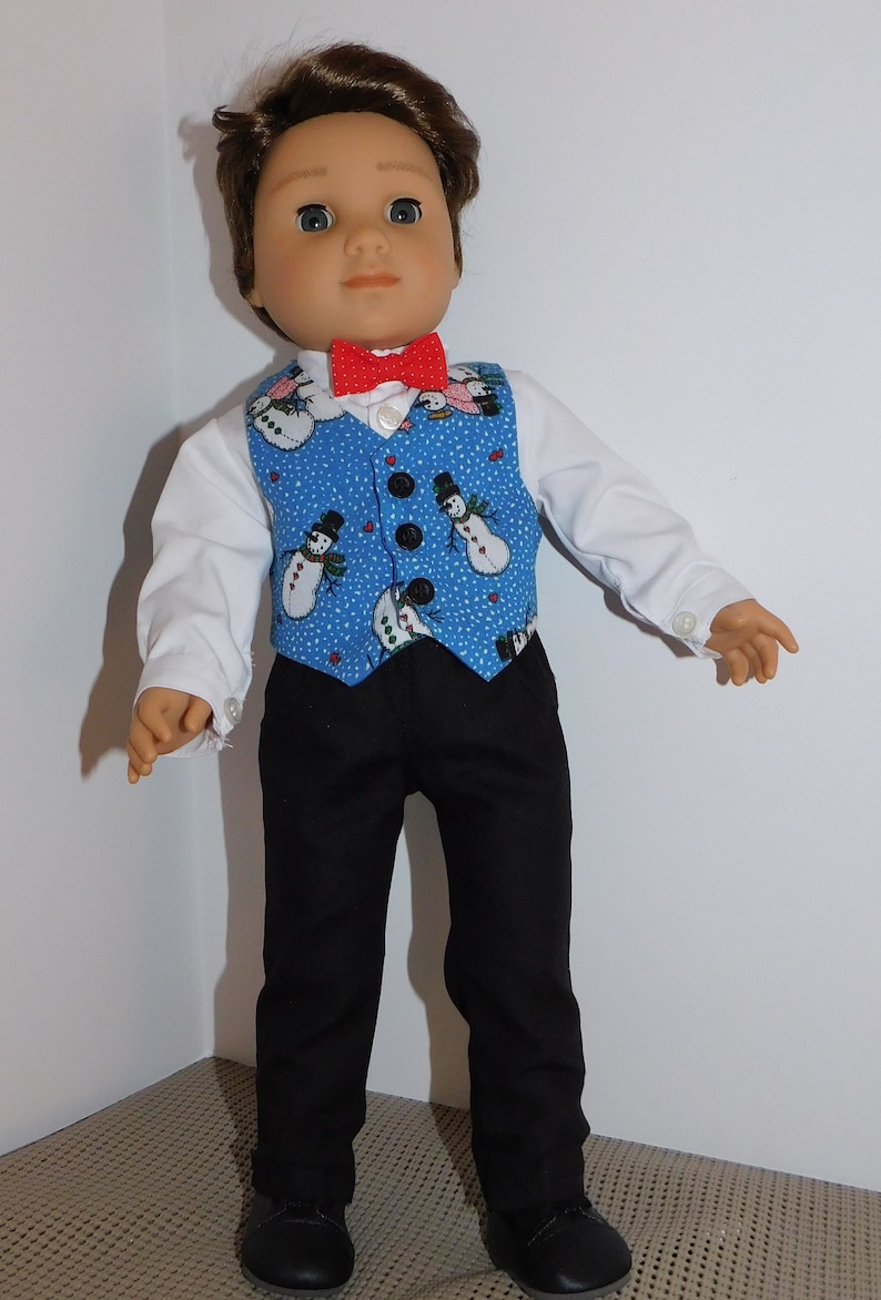 May include: A doll wearing a blue vest with a snowman pattern, a red bow tie, a white shirt, black pants, and black shoes.