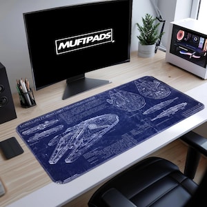 Puede incluir: Una alfombrilla de escritorio rectangular azul con esquemas blancos del Halcón Milenario. La alfombrilla tiene el texto "CORELLIAN YT-1300 LIGHT FREIGHTER (MACCADON)". El monitor muestra el texto "MUFTPADS".
