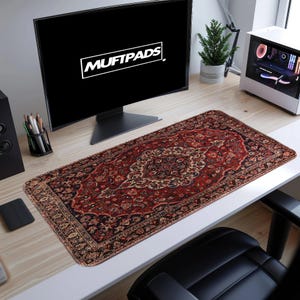 May include: A rectangular desk mat with a Persian rug design. The mat features a deep red background with intricate floral and geometric patterns in shades of beige, navy, and gold. The text "MUFTPADS" is displayed on the computer screen.