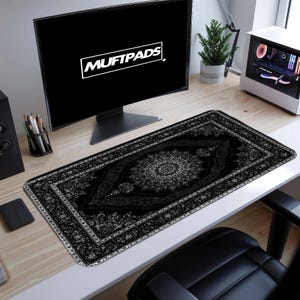 May include: A black and gray rectangular desk mat with an ornate rug design. The mat features a central medallion pattern and a border with floral motifs. The text "MUFTPADS" is displayed on a computer monitor in the background.