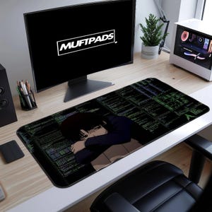 May include: Black rectangular desk mat with a manga-style illustration of a person and a dark green code background. The mat is on a light wood desk with a monitor displaying "MUFTPADS".