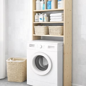 May include: A white washing machine with a wooden shelf unit above it. The shelves hold laundry supplies, towels, and woven baskets. A matching basket sits on the floor. The unit is in a bathroom with white tile.