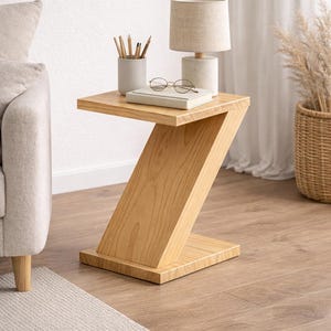 Puede incluir: Mesa auxiliar de madera clara con un diseño en zigzag. La mesa sostiene una lámpara pequeña, un libro, gafas y un portalápices. La mesa está sobre un suelo de madera, junto a un sofá y una alfombra. Medidas en cm.