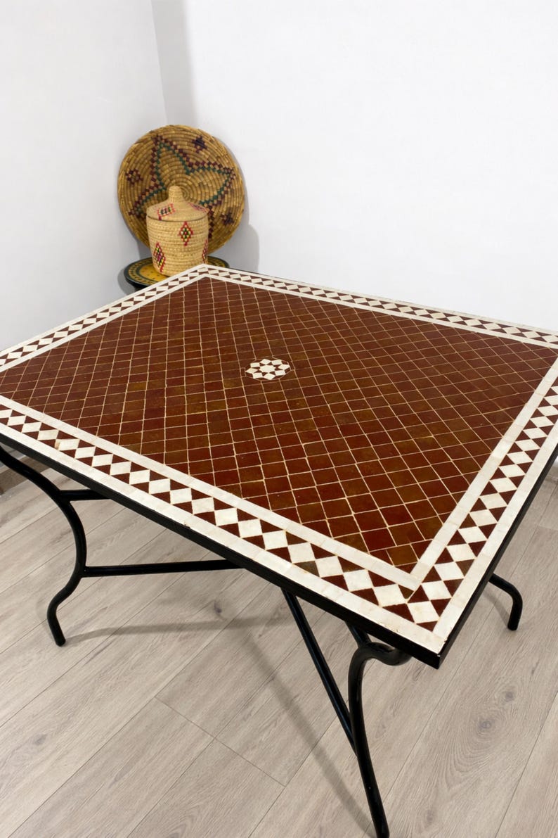 K&ouml;nnte beinhalten: Quadratischer Mosaiktisch mit braunem und wei&szlig;em geometrischem Muster. Der Tisch hat ein schwarzes Metallgestell und Beine. Dekorative gewebte K&ouml;rbe sind im Hintergrund.