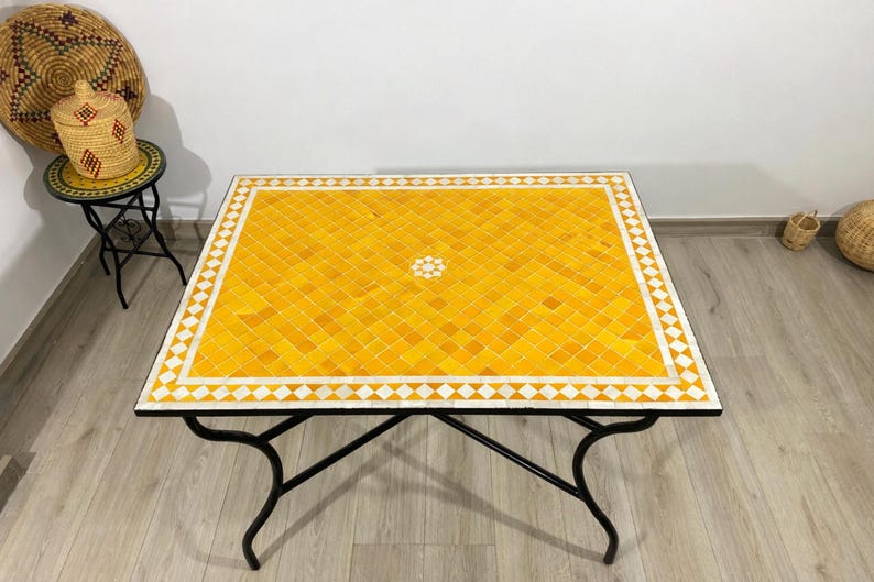 K&ouml;nnte beinhalten: Ein quadratischer Couchtisch mit einer gelben Fliesenmosaikplatte und einem wei&szlig;en Diamantrand. Der Tisch hat ein schwarzes Metallgestell und Beine. Der Tisch ist etwa 99 cm gro&szlig;.