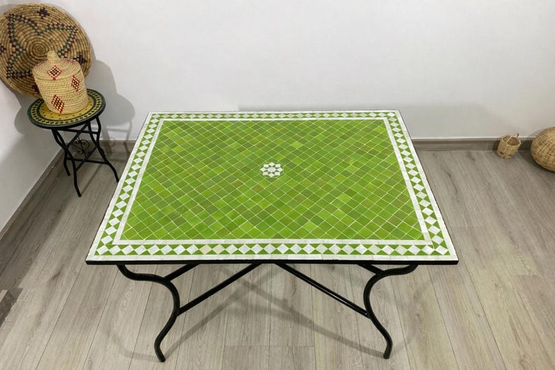K&ouml;nnte beinhalten: Quadratischer Couchtisch mit einer gr&uuml;nen Mosaikfliesenplatte und einem wei&szlig;en Diamantrand. Der Tisch hat ein schwarzes Metallgestell mit geschwungenen Beinen. Der Tisch ist etwa 91 cm gro&szlig;.