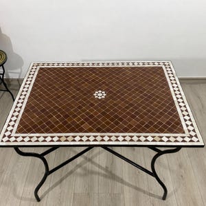 May include: Square mosaic tile coffee table with a brown and white geometric pattern. The table has a black metal frame with curved legs. The tabletop is made of small, square tiles in shades of brown and white, arranged in a diamond pattern.