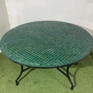 Peut inclure: Table ronde d'extérieur avec un dessus en mosaïque verte. Le cadre est en métal noir avec des pieds incurvés. Le motif de la mosaïque est géométrique et répétitif. Une pièce élégante pour un patio ou un jardin, environ 120 cm de diamètre.