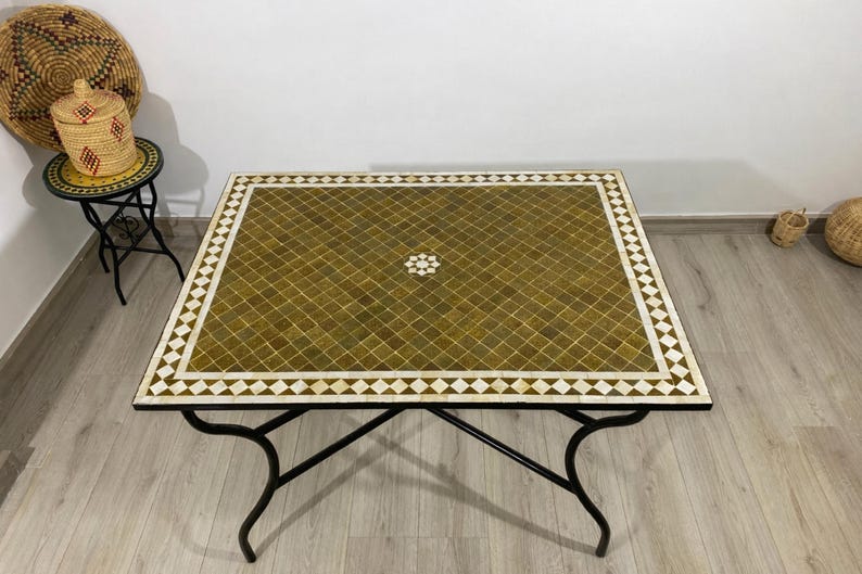 K&ouml;nnte beinhalten: Quadratischer Couchtisch mit Mosaikfliesen in Olivgr&uuml;n und Wei&szlig;. Der Tisch hat ein schwarzes Metallgestell mit geschwungenen Beinen. Das Mosaikdesign zeigt ein zentrales Blumenmuster.