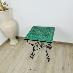 May include: A square side table with a mosaic tile top in shades of green. The table has a black wrought iron base with decorative scrollwork. The table is approximately 20 inches square and 20 inches high.