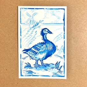 May include: A blue and white watercolor illustration of a duck standing in a field with a windmill in the background.
